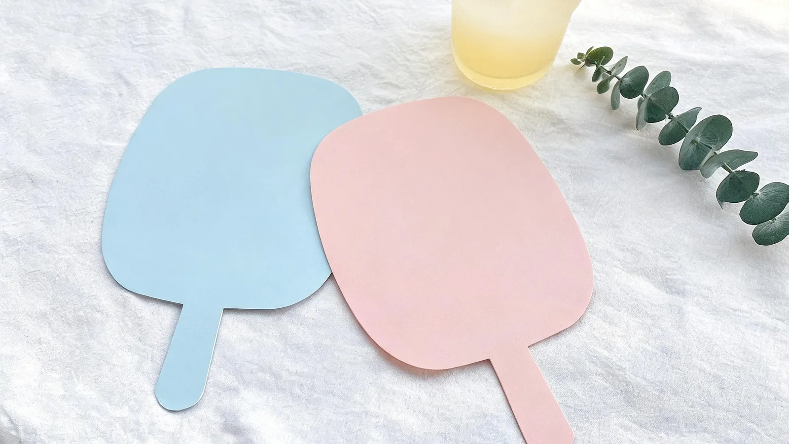 Illustration: a blank blue paddle and a blank pink paddle on a white cloth beside a eucalyptus sprig and a frosted yellow glass.